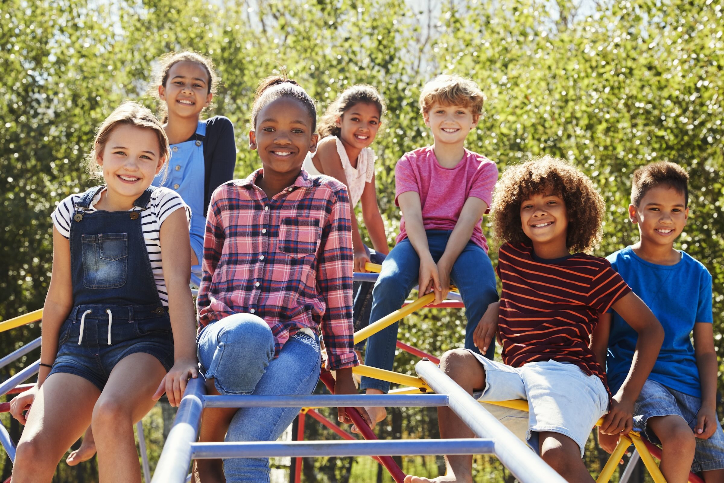 Diverse group of children playing together on playground equipment - healthy, active kids cared for by Muskegon Pediatrics
